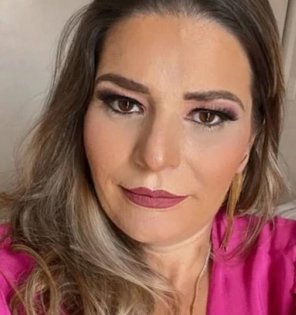 A woman with long brown hair, wearing a pink top and bold eye makeup.