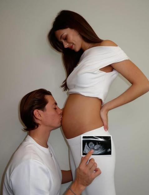 Sam Vanderpump kisses Alice Yaxley's pregnant belly while holding up a sonogram.
