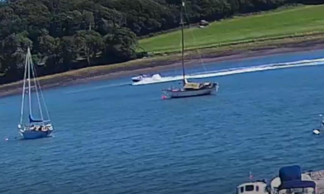 A speedboat leaving a white wake in a river with sailboats.