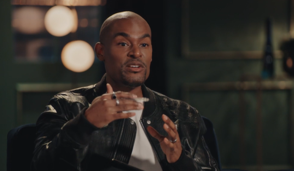 Paul C Brunson, wearing a black leather jacket, speaking animatedly with his hands.