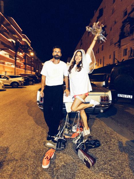 Melanie C and Chris looking at the camera, leaning on a car with strings of sneakers around them.