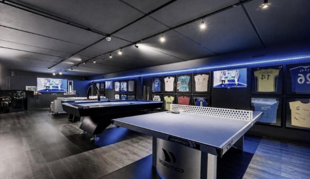 A recreation room with a pool table, ping-pong table, arcade games, and framed sports jerseys.