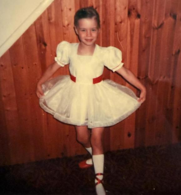 Denise Van Outen dancing as a child in a white dress with a red sash.