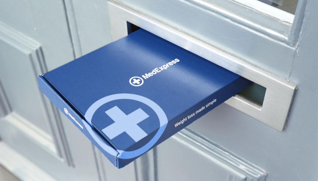 A blue MedExpress box being delivered through a letterbox, with "Weight loss made simple" printed on it.