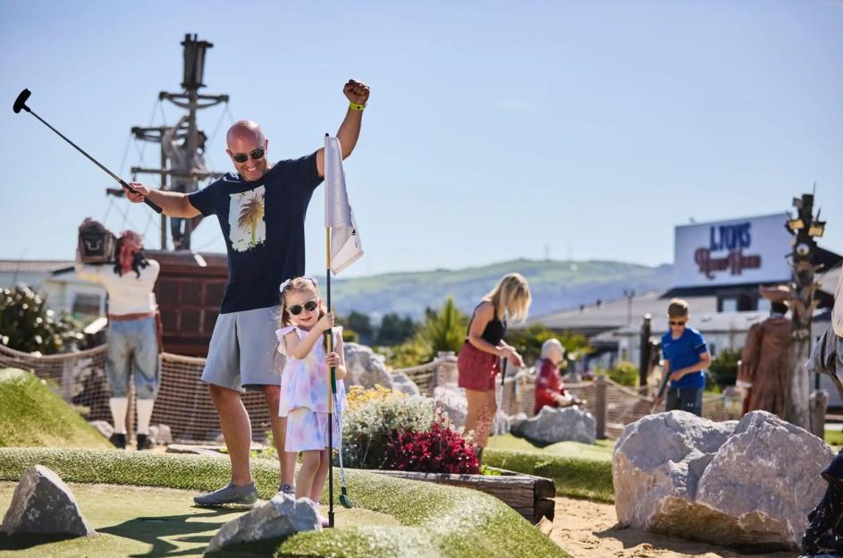 A man and a child playing miniature golf at Lyons Holiday Park.