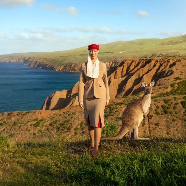 An Emirates air hostess in uniform and a kangaroo stand on a cliff overlooking the ocean.