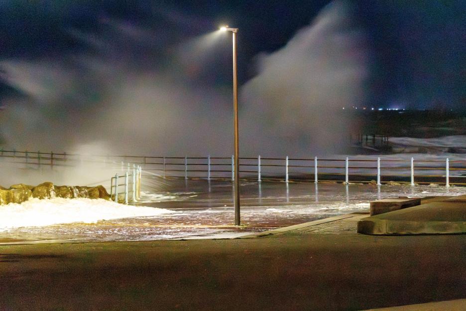 Waves breaking over sea defenses on the promenade at Heysham during high tide at night.