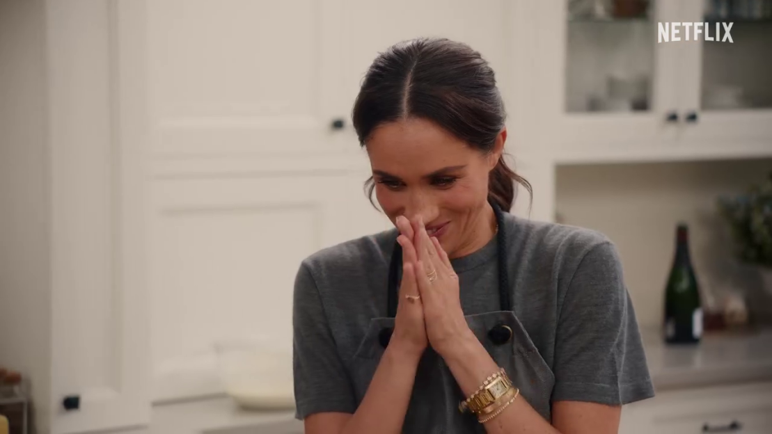 Meghan Markle smiling with hands clasped.