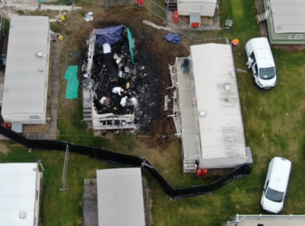 Aerial view of a burnt caravan next to other caravans in a park, with debris scattered on the ground.