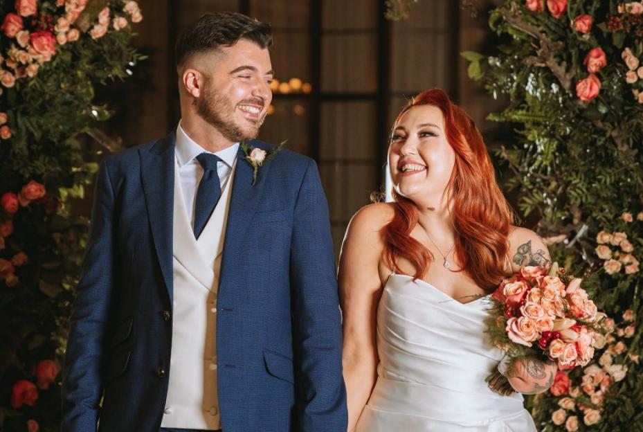 A smiling bride and groom facing each other, surrounded by flowers.