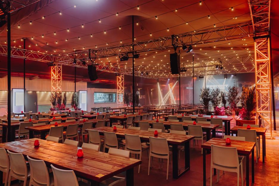 An empty dining hall at a London rooftop attraction with string lights, red decor, and stage lighting.
