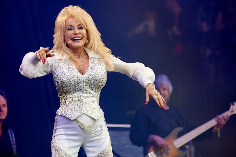 Dolly Parton performing at the Glastonbury Festival in a white, rhinestone-studded outfit.