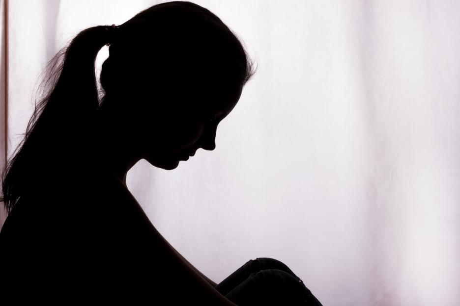 Silhouette of a young woman sitting and looking down in despair.