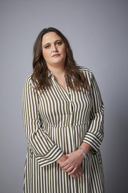 Chanel Mare, a woman with long brown hair, wearing a striped dress and a blue beaded bracelet, posing for a portrait.