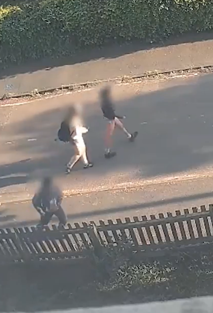 Three blurry figures of youths, two walking along a street, one crouching behind a fence.