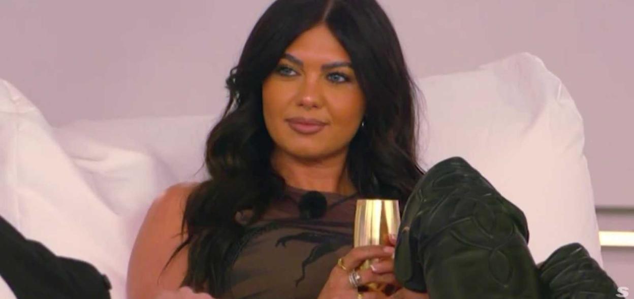 Woman in brown top with gold drink and black boots.