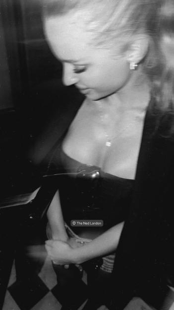 A blurry, black and white photo of a woman in a low-cut top, holding a phone with a "The Ned London" tag.