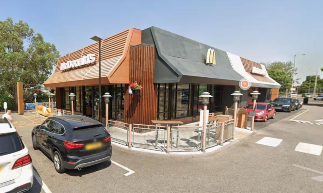 A McDonald's restaurant with a drive-thru, surrounded by cars and trees on a sunny day.