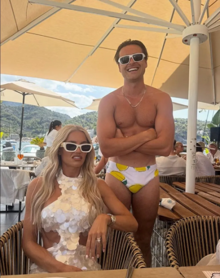 A man in a lemon-print swimsuit smiles behind a woman in a sequined dress and sunglasses.