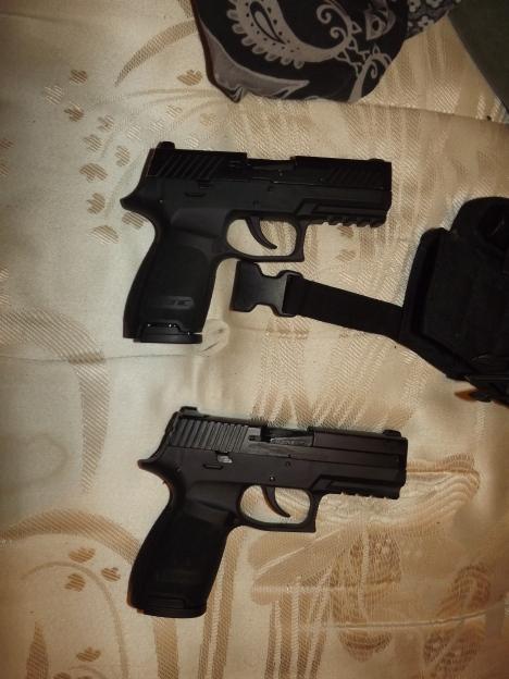 Two black handguns lying on a patterned beige surface, with a black strap partially visible.