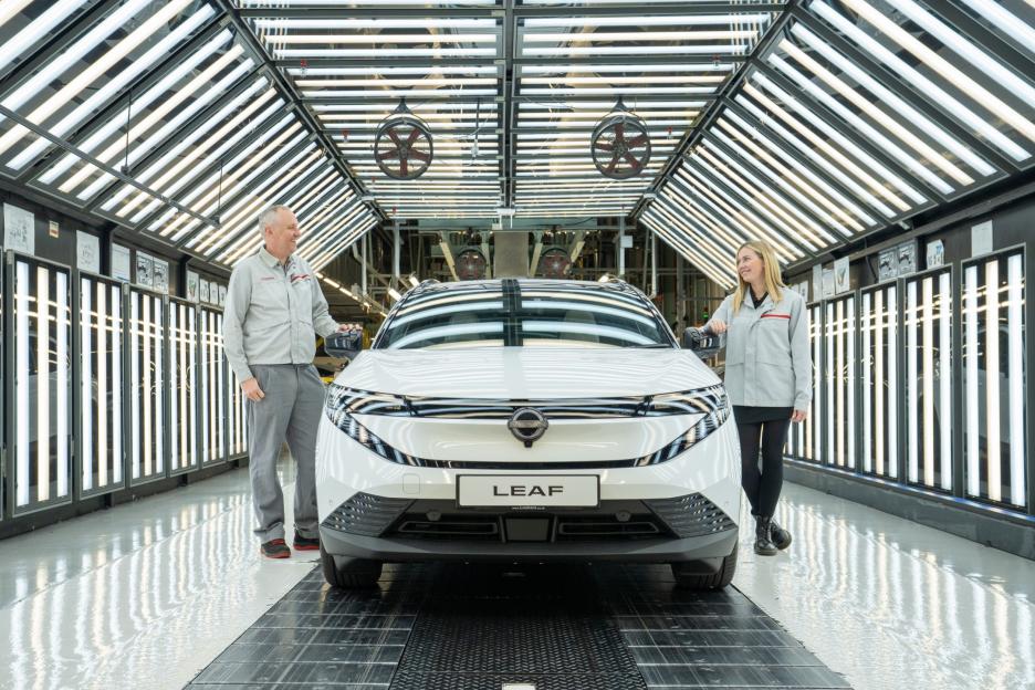 Two Nissan employees with a white Nissan Leaf in a brightly lit factory.