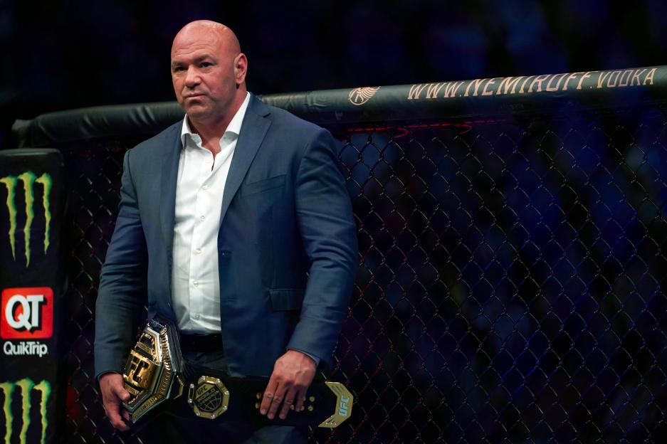 UFC President Dana White in a suit holding the UFC lightweight championship belt.