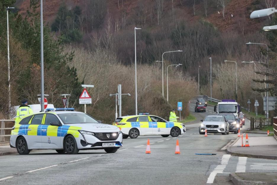Police cars and officers blocking a road, diverting traffic.