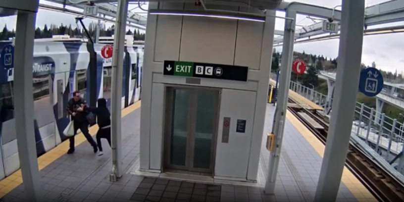 A man in a black hoodie shoves another man towards a moving train on a platform.