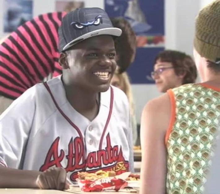 Daniel Kaluuya as Posh Kenneth in "Skins," wearing an Atlanta Braves jersey and a baseball cap, smiling at another person.