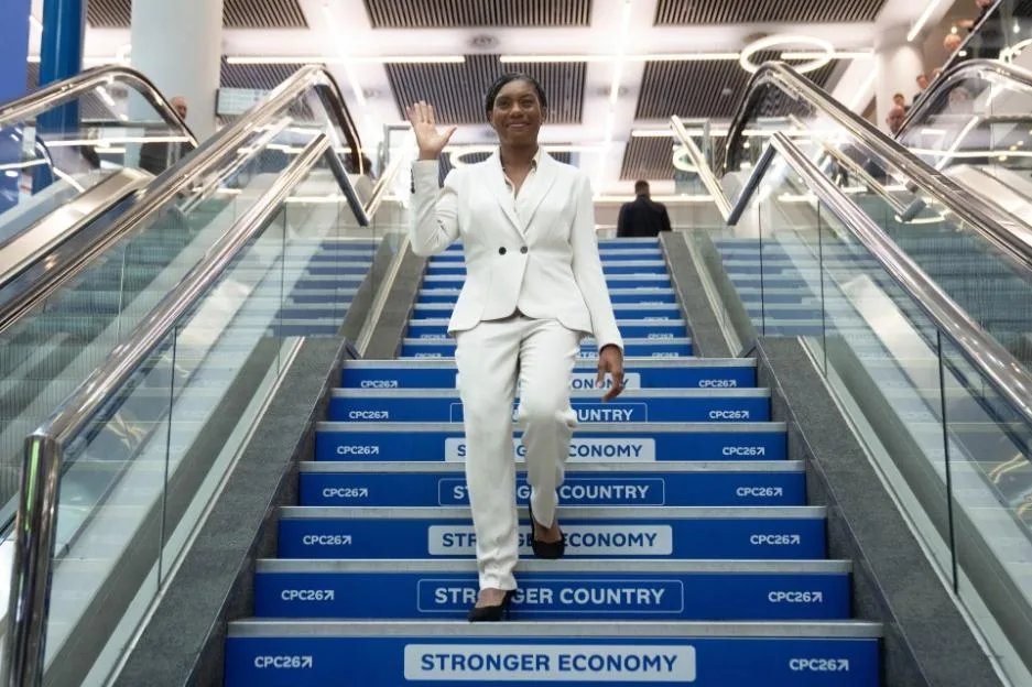 Conservative Party leader Kemi Badenoch waves while walking down stairs.