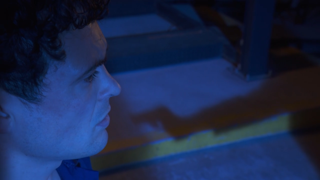 Close-up of Jonny Labey as Rex on Hollyoaks, his face illuminated by a blue light.