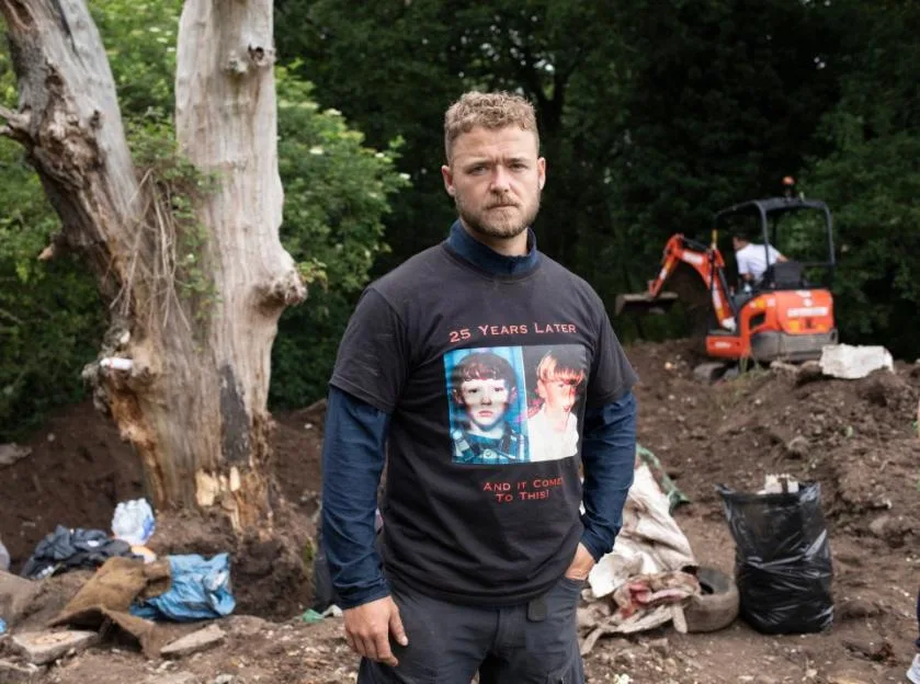 A man in a "25 Years Later" t-shirt stands at a missing person dig site in Solihull.