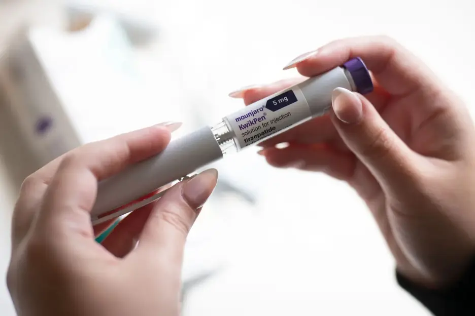 A person's hands holding a Mounjaro KwikPen for injection.