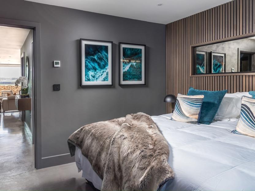 A bedroom in a seaside apartment with two framed ocean prints, a large bed with a fur throw, and blue pillows.