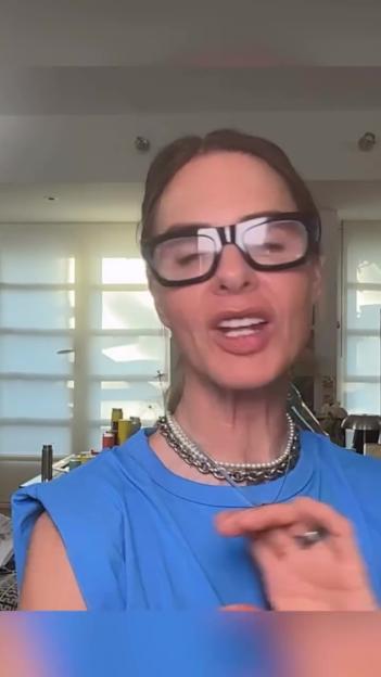 Trinny Woodall wearing glasses, blue top and necklaces while speaking.