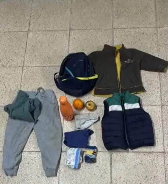 Items left for children in the forest, including clothes, a backpack, fruit, and a drink.