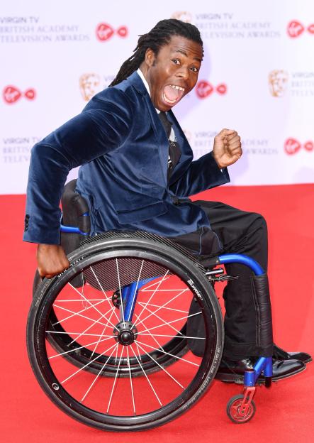 Ade Adepitan posing in his wheelchair on the red carpet at the Virgin TV British Academy Television Awards.