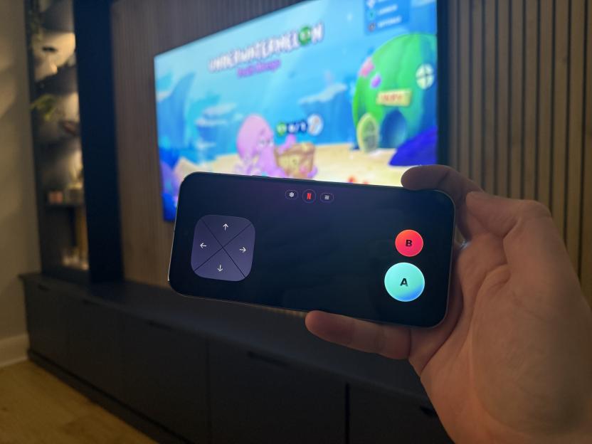 A hand holding a smartphone used as a game controller for a video game displayed on a TV.