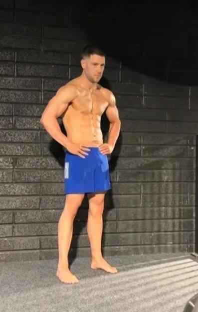 A shirtless man in blue shorts posing for a photo.