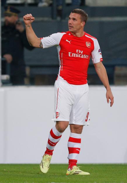 Lukas Podolski, in a red and white Arsenal uniform, raises his right arm with a closed fist.