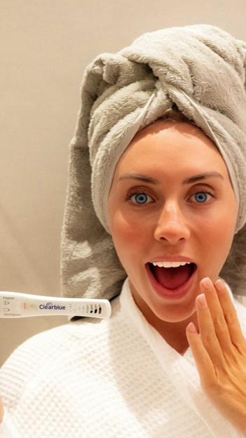 Bonnie Blue holding a Clearblue pregnancy test with a surprised expression.