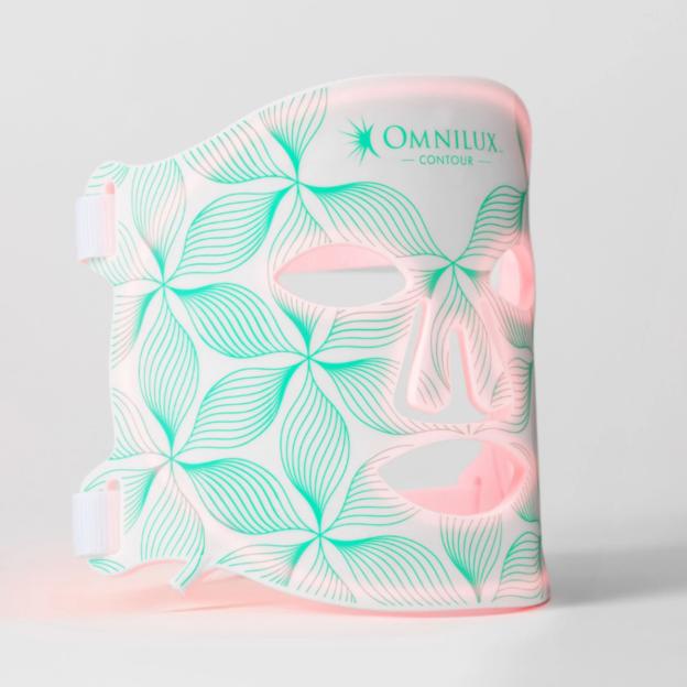 Omnilux Contour face mask with green floral patterns and pink light glowing through it.