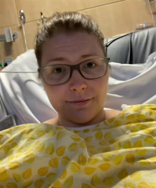 A young woman in a hospital gown looks directly at the camera.