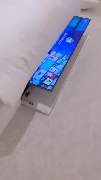 A television screen showing Discovery+ content retracting into a white bed frame.