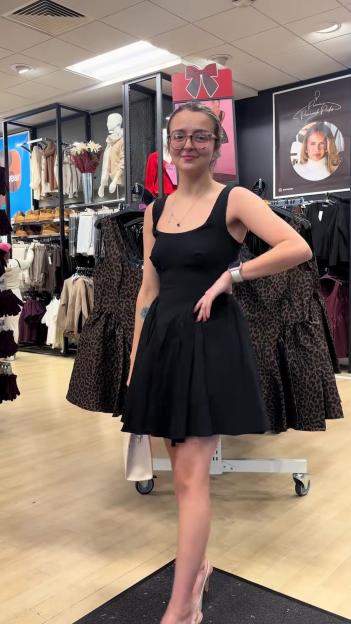 A woman poses in a black dress in a clothing store.