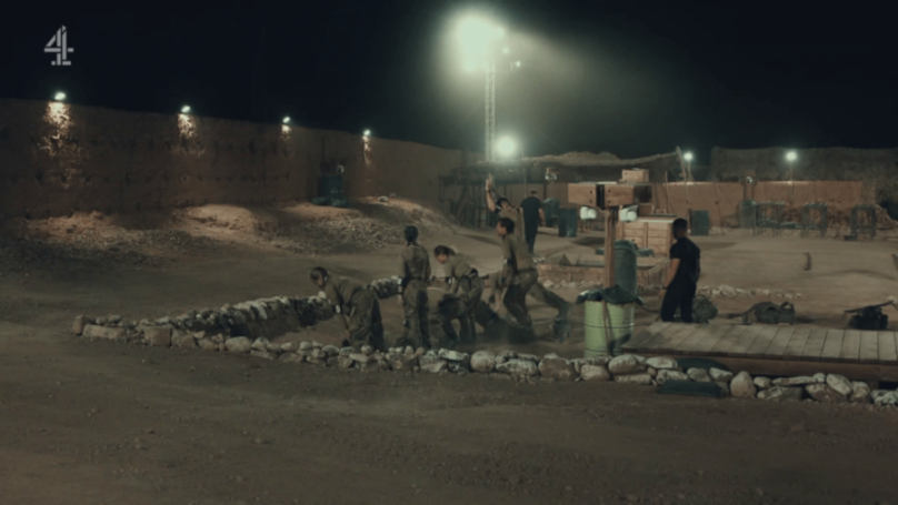 People in military-style uniforms performing an exercise in a sandy, outdoor training area at night.