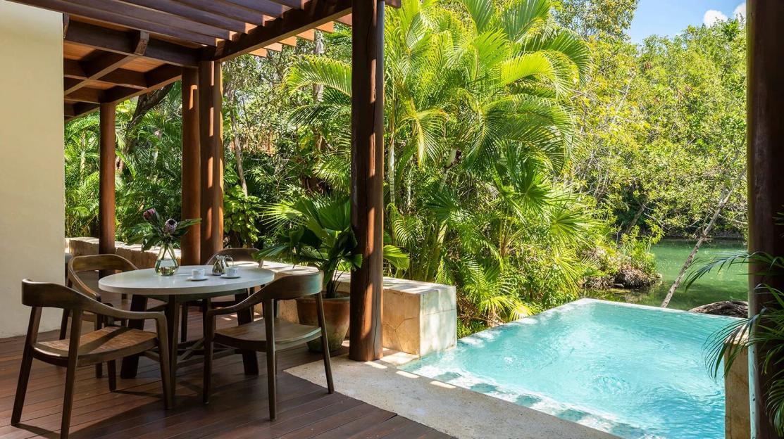 A hotel patio with a table and chairs, a small pool, and lush vegetation.