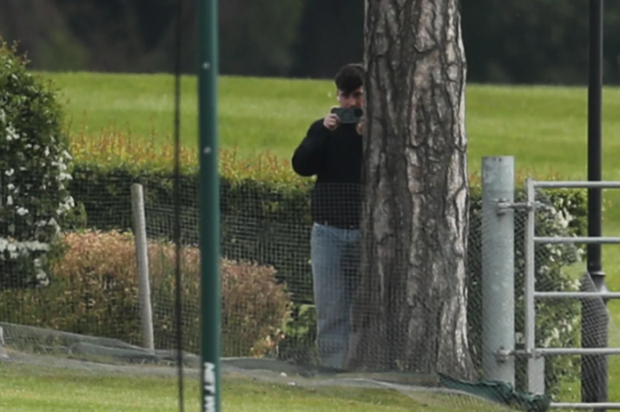 Person hiding behind a tree and filming with a smartphone.