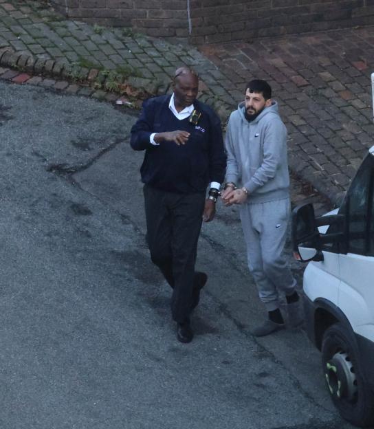 Albert Matraxhiu in handcuffs, being escorted by a security guard.