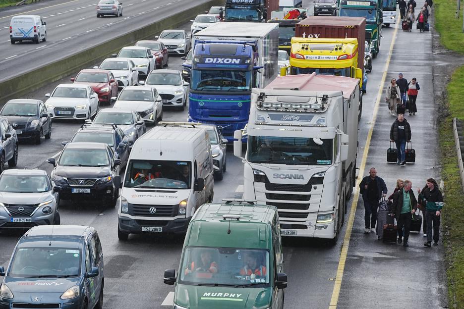 People with luggage walking along a busy motorway with heavy traffic due to a fuel protest.